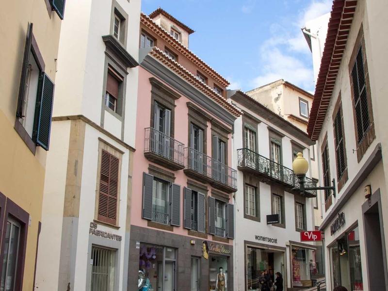 Nauwe, kronkelige straat met kinderkopjes en meerlaagse gebouwen en winkels.