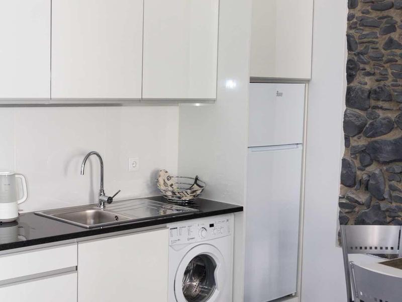 Moderne witte keuken met wasmachine, koelkast en zwarte werkbladen.