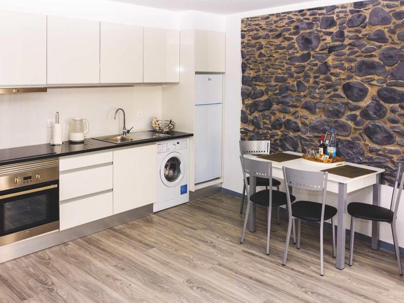 Moderne kleine keuken met witte kasten, wasmachine en eettafel bij stenen muur.