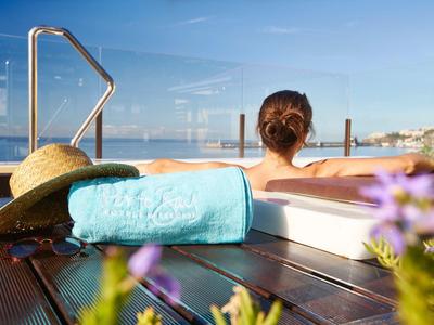 Donna rilassata in una vasca idromassaggio esterna con asciugamano e cappello da sole sul ponte in legno.