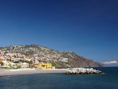 Spiaggia e porto con case su una collina costiera soleggiata sotto un cielo blu chiaro