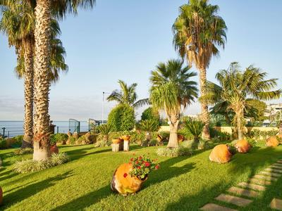 Giardino verde sul mare con palme, sculture rotonde e cielo limpido.