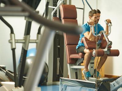 Muž cvičí na stroji v světlé posilovně.