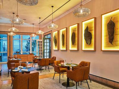 Ristorante d'hotel elegante con poltrone marroni, opere d'arte illuminate e lampade a sospensione moderne.