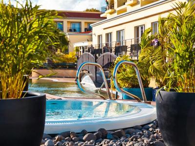 Vasca idromassaggio esterna di un hotel con piante e piscina sullo sfondo.