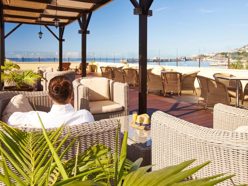 Vista da una lounge coperta con mobili in vimini verso il mare e la spiaggia al sole.