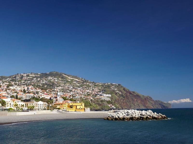Spiaggia e porto con case su una collina costiera soleggiata sotto un cielo blu chiaro