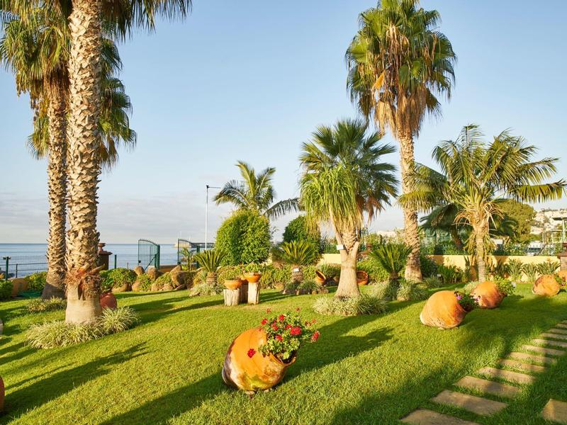 Giardino verde sul mare con palme, sculture rotonde e cielo limpido.