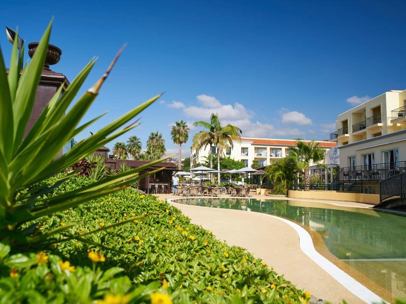 Struttura alberghiera con piscina, piante verdi e cielo blu soleggiato