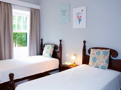 Una stanza luminosa con due letti singoli, cuscini e una finestra con vista sul verde.