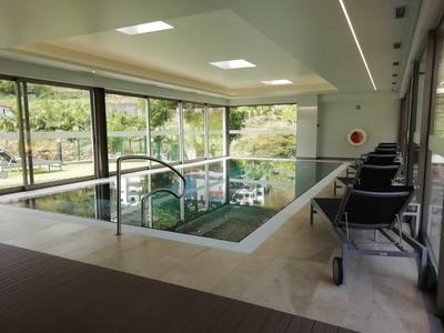 Piscina coperta moderna con grandi finestre e sedie nere lungo il bordo.