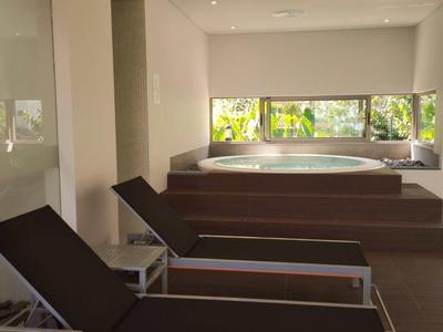 Area benessere luminosa con vasca idromassaggio e due lettini, grandi finestre con vista sul verde.