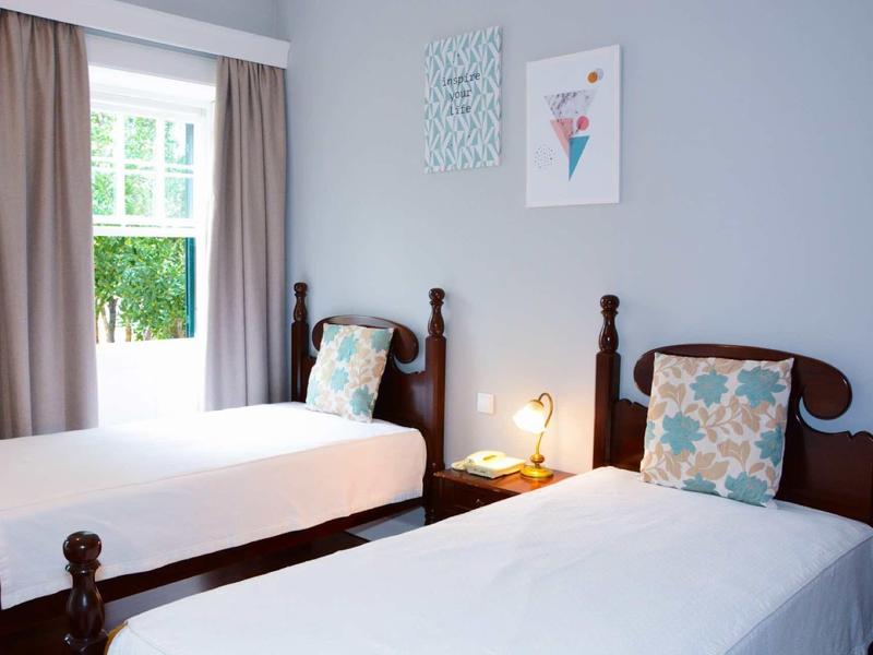 Una stanza luminosa con due letti singoli, cuscini e una finestra con vista sul verde.