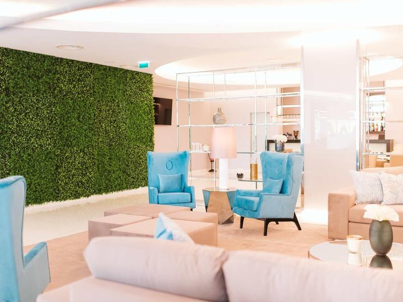 Heller, moderner Wohnbereich mit blauen Sesseln, Sofas und grüner Pflanzenwand.