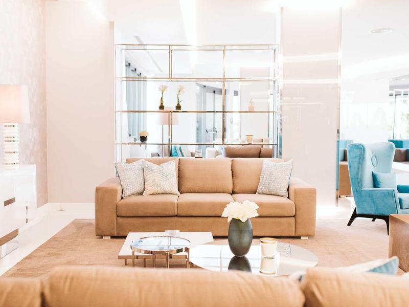 Heller Wohnraum mit beigen Sofas, Glastisch, weißen Wänden und blauen Sesseln.