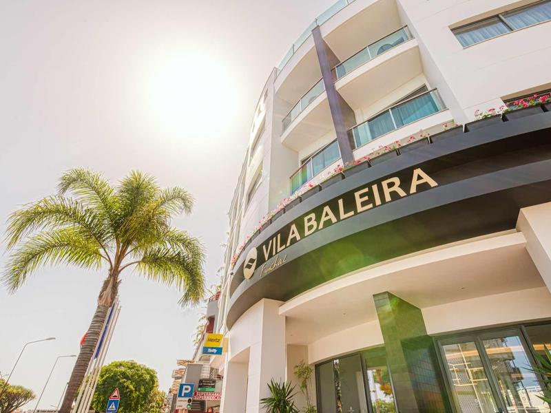 Moderner mehrstöckiger Gebäudekomplex mit rundem Balkon und Palmen im sonnigen Freiluftbereich.