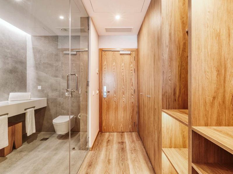 Moderner Flur mit Holzvertäfelung, Glasdusche rechts, Waschbecken links und hellen Beleuchtungselementen.