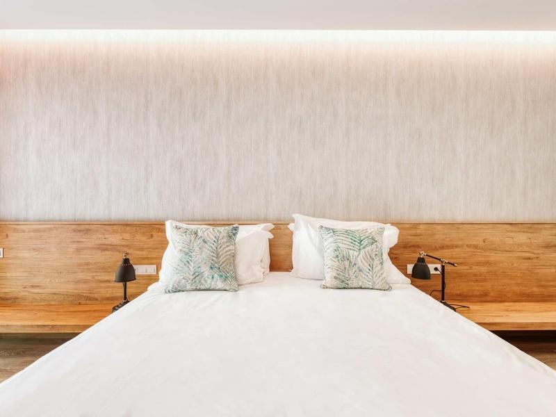 Modernes Schlafzimmer mit großem Bett, Holzkopfteil, zwei Kissen und integrierter Beleuchtung.