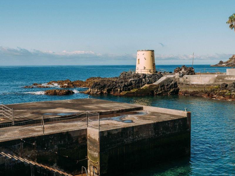 Vecchia torre in pietra su rocce al largo di un mare limpido e blu con cielo nuvoloso.