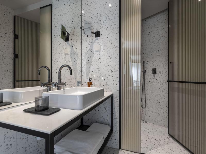 Bagno moderno dell'hotel con lavabo, specchio e doccia separata in tonalità chiare.