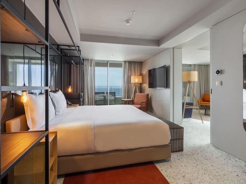 Camera d'hotel moderna con letto matrimoniale, balcone e vista sul mare.