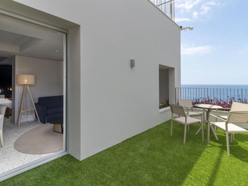 Terrazza con sedie e tavolo su prato artificiale con vista sul mare in una giornata di sole.