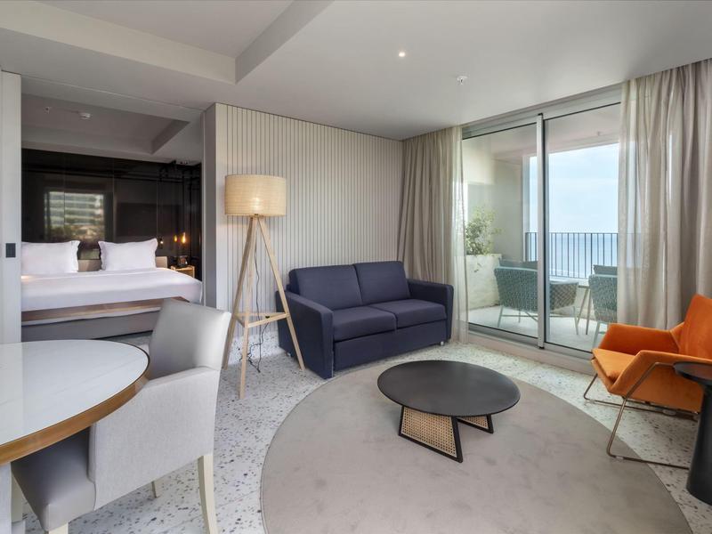 Camera d'hotel moderna con soggiorno, balcone e vista mare.