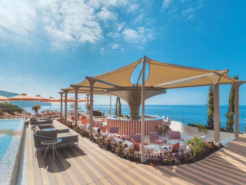 Bar di lusso con vele ombreggianti accanto alla piscina con vista mare e cielo azzurro.