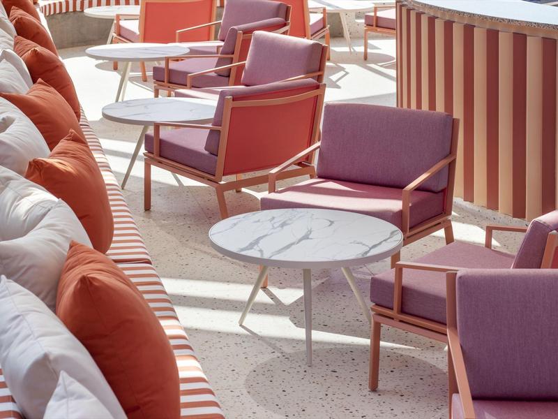 Area terrazza con cuscini a righe, poltrone viola e tavoli rotondi bianchi.