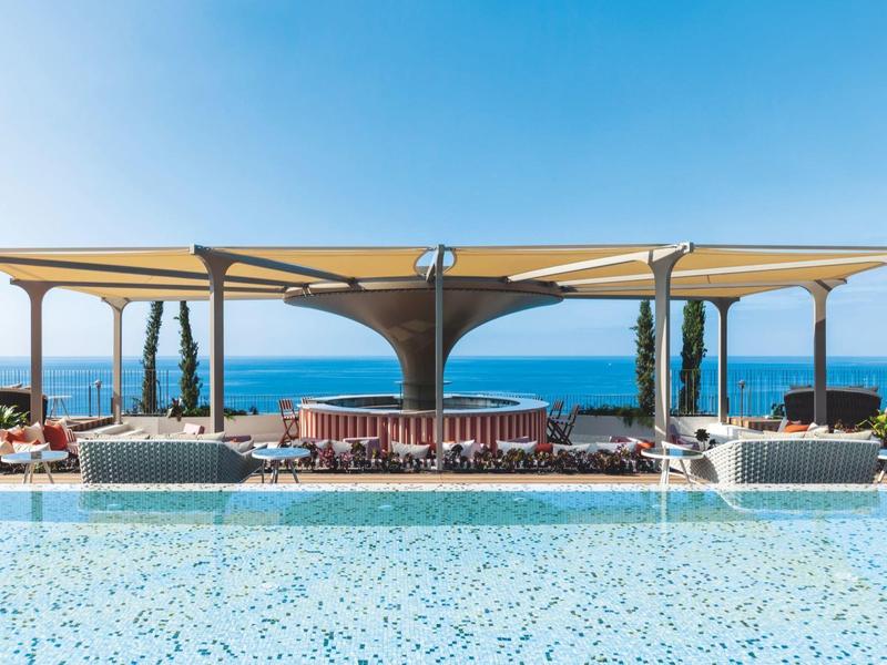 Area piscina moderna con lettini e vista sul mare sotto un cielo limpido.