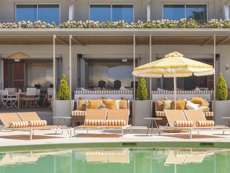 Comode poltrone con ombrelloni accanto a una piscina davanti a un edificio alberghiero