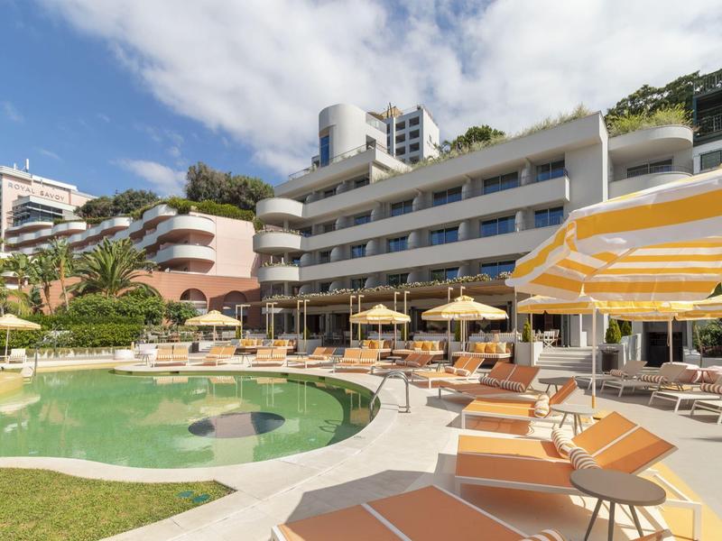 Area piscina di un hotel moderno con lettini e ombrelloni sotto un cielo azzurro.