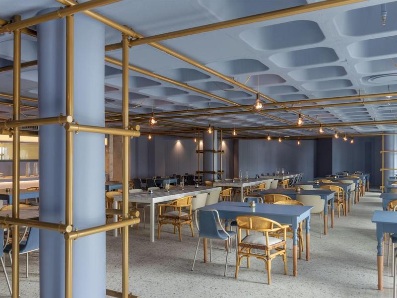 Sala da pranzo moderna con sedie blu e tavoli in legno in un ambiente luminoso.