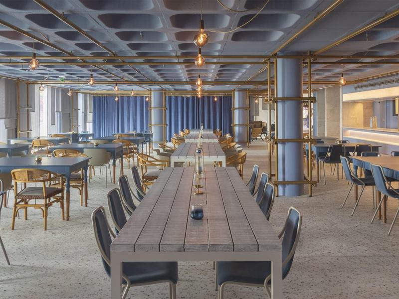 Ampia sala da pranzo moderna con lungo tavolo di legno e numerose sedie in ambiente luminoso.