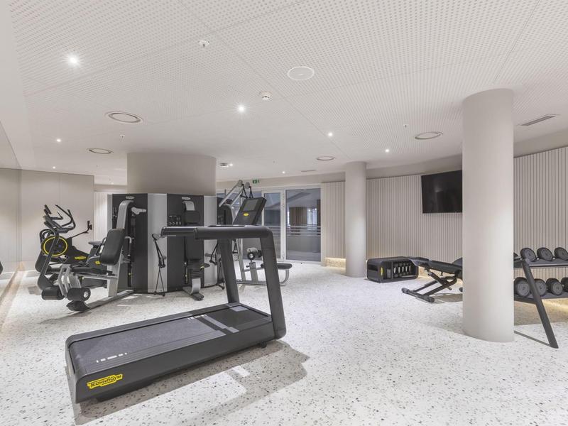 Palestra moderna con tapis roulant, biciclette e pesi in una stanza luminosa.