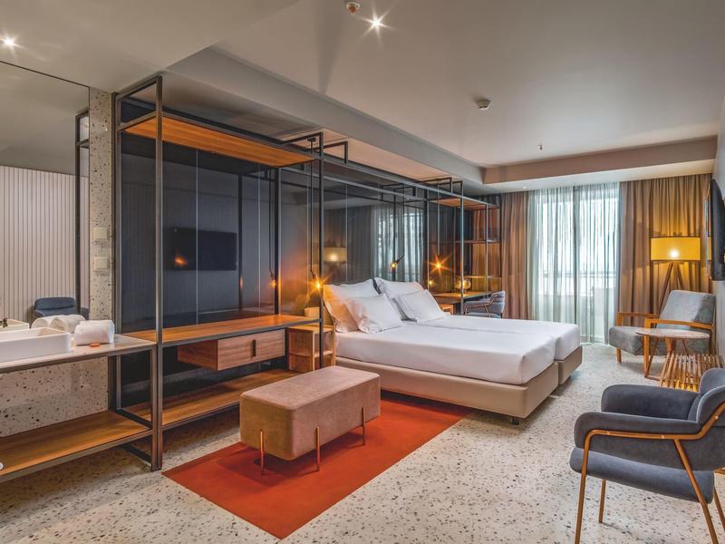 Camera d'hotel moderna con due letti, mobili eleganti e grandi finestre.