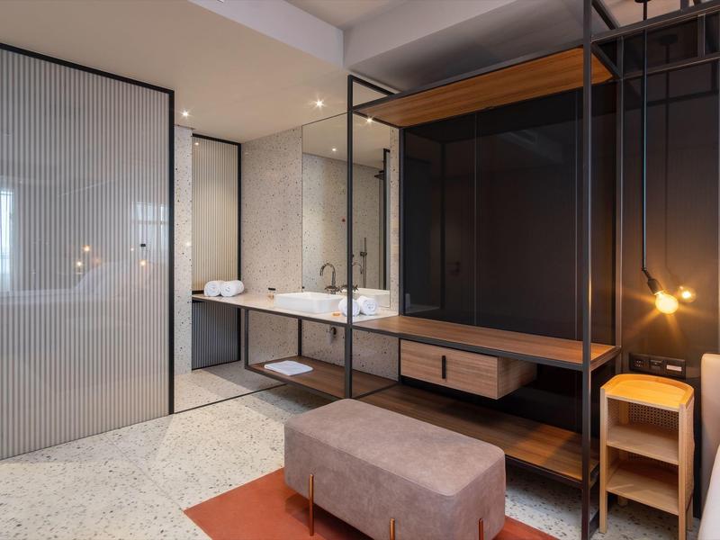 Bagno moderno con doppio lavabo, doccia in vetro e panca in tonalità calde.