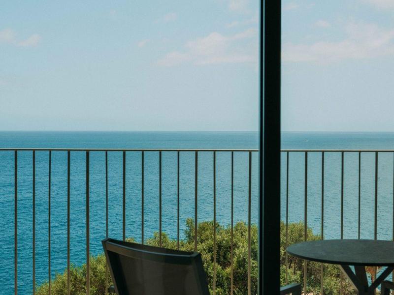 Balcone con sedia e tavolo che si affaccia sul mare blu sotto un cielo nuvoloso.