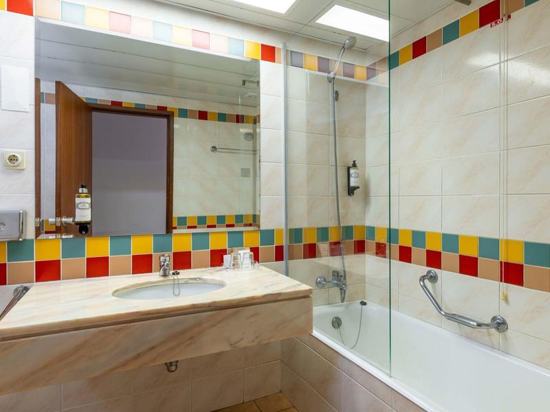 Bagno luminoso piastrellato con piastrelle colorate, grande specchio e vasca con parete doccia.