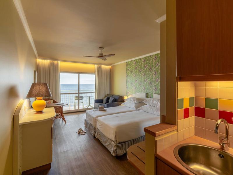 Camera d'hotel moderna con letto matrimoniale, zona salotto e vista mare da grandi finestre.