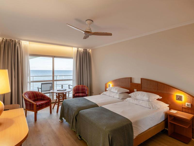 Camera d'hotel moderna con due letti singoli, vista mare e area salotto accogliente.