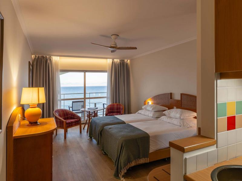 Camera d'hotel con due letti, poltrone e vista mare attraverso grandi finestre