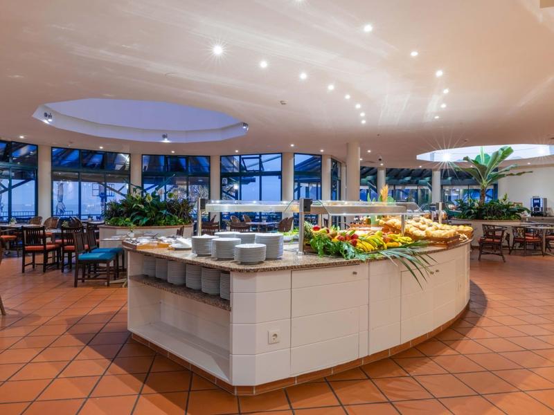 Ampia zona buffet con banconi rotondi, tavoli apparecchiati e grandi finestre in un ristorante.