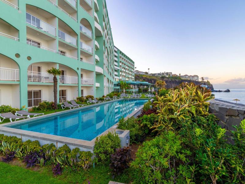 Piscina moderna dell'hotel accanto a un edificio di più piani con vista sul mare.