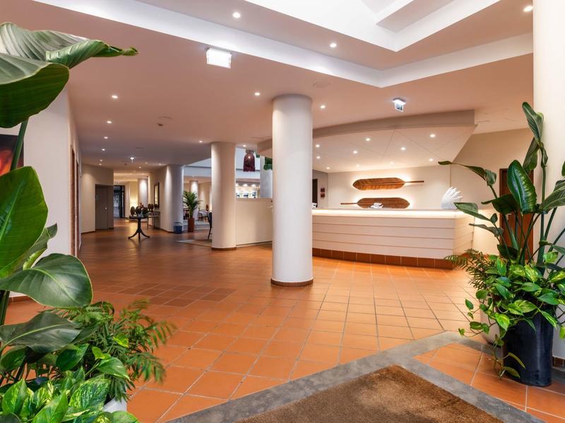 Luminosa hall dell'hotel con piante e reception moderna in toni caldi.