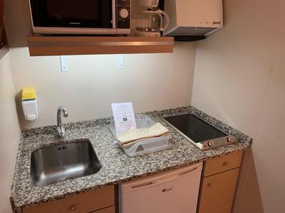 Piccola angolo cottura con lavello, microonde, stoviglie e piano in granito.