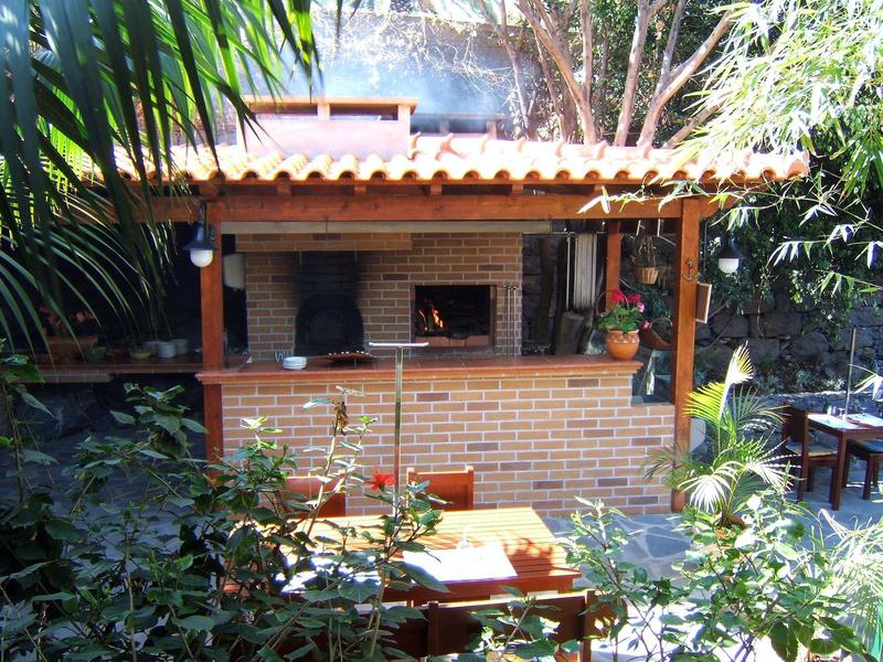 Area barbecue esterna con barbecue in mattoni, tavolo in legno e piante verdi