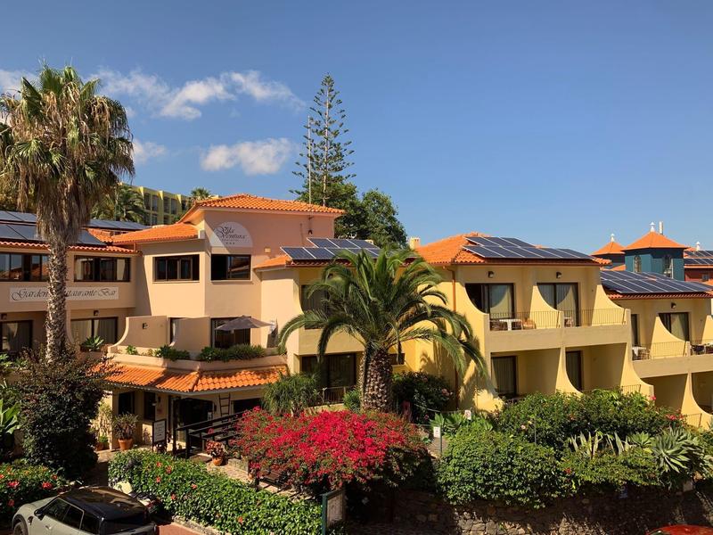 Hotel con tetti arancioni circondato da vegetazione lussureggiante e palme sotto un cielo blu.