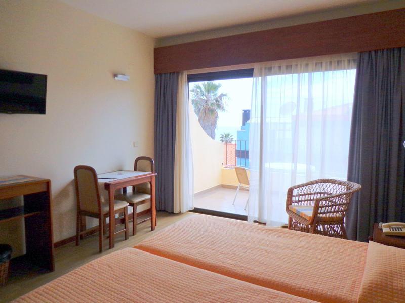 Camera d'hotel luminosa con due letti, scrivania, sedie e balcone con vista esterna.