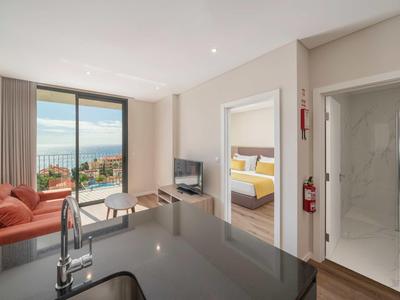 Moderner Wohnraum mit offener Küche, Sofa, Fernseher, Schlafzimmer und Bad mit großer Fensterfront und Meerblick.